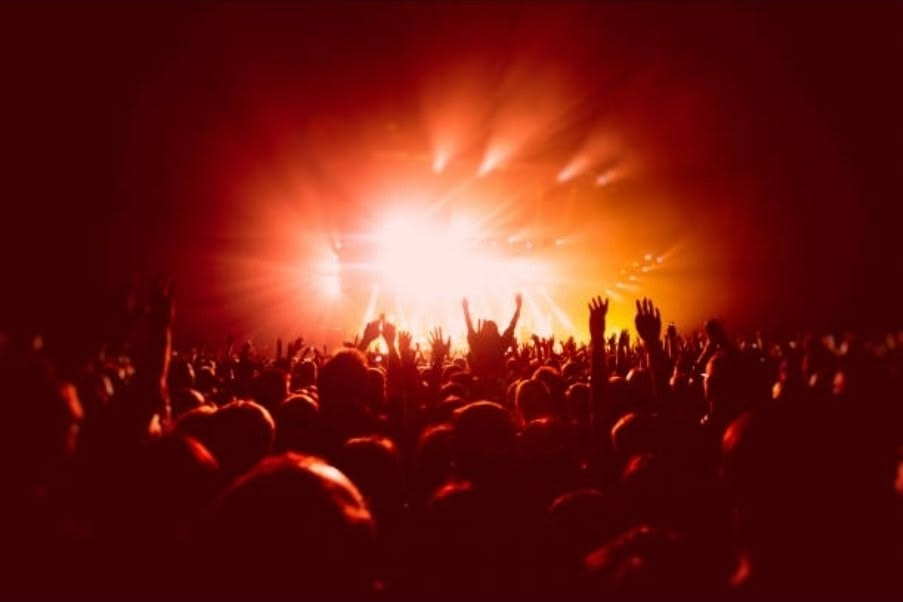 A crowd swaying in warm haze on a dance floor, amber light beams cutting through gentle smoke.