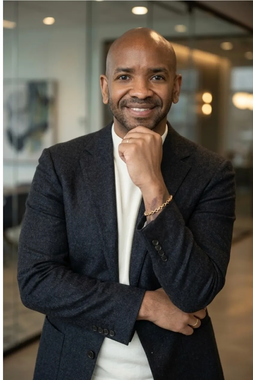 Solomon E. Stretch, LPC, smiling with a hand at his chin, wearing a dark blazer over a white shirt in a warmly lit office.