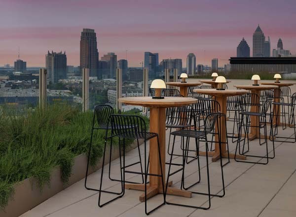 Set and setting for a cannabis session: a rooftop patio at dusk with wooden tables, warm lamps, and the Atlanta skyline behind.